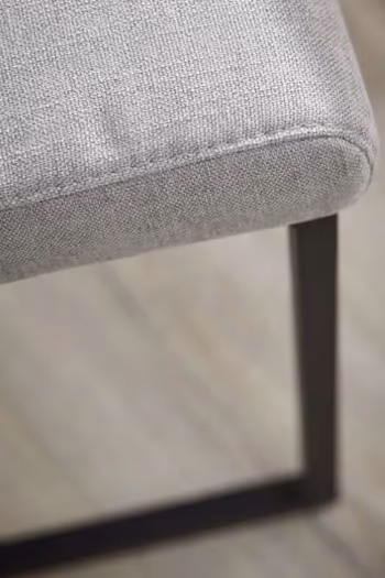 Teile der Sitzfläche eines grauen Stuhls mit schwarzem Fußgestell.