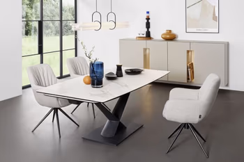 Drei bequem gepolsterte beige Armlehnstühle, die eine moderne Faltenbildung an der Rückenlehne haben und ein schwarzes Metallgestell und um einen modernen Keramik Esstisch in einem hellen Raum stehen.