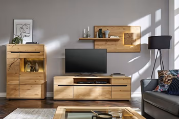Helle Wohnwand aus Massivholz bestehend aus Vitrine mit Glaseinsatz, TV-Board und hängendes Wandregal in einem gemütlichen Raum.