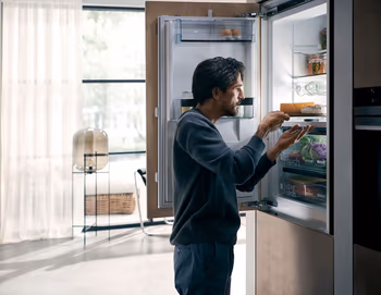 Mann steht vor dem geöffnetem Kühlschrank und nimmt etwas.