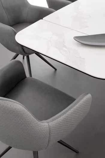 Ansicht eines grauen Design Armlehnstuhls, der auf der Rückseite mit Stoff und innen mit Leder bezogen ist und an der Stirnseite eines weißen Designer Esstisches steht.