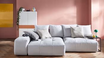 Hellgraues bodentiefes Sofa mit gemütlichen Kissen am Rücken. 