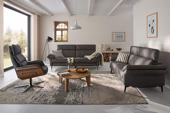 Zwei graue Design Ledersofa Garnituren mit hoher Rückenlehne und Relaxsessel in einem hellen Raum. 