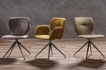 Drei Esszimmerstühle mit schwarzem Metallgestell nebeneinander, der linke hat einen Bezug aus Leder in taupe, der mittlere in gelbem Leder mit Armlehne und der rechte in grünem Stoff.