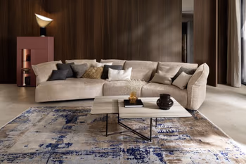 Beiges Designersofa, das trapezförmig verläuft, dekoriert mit mehreren Kissen in Beige, grau und weiß.