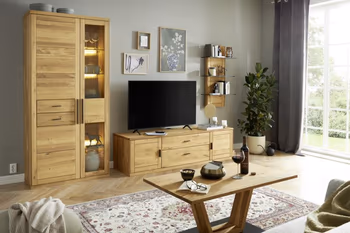 Wohnwand aus hellem Massivholz bestehend aus Wandregal, TV-Board mit Glastür, Sideboard mit Glaseinstätzen und Vitrine mit Glaseinsatz in einem hellen Raum mit dazu passendem Couchtisch.