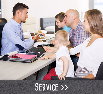 Beratungssituation mit einer Familie am Tisch, ein Verkäufer zeigt Stoffmuster.