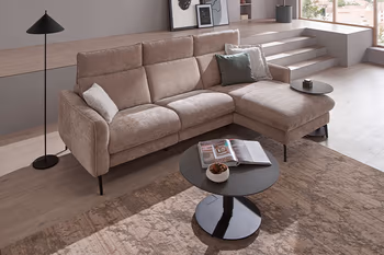 Runder schwarzer höhenverstellbarer Couchtisch vor einem beigen Ecksofa.