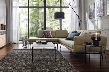 Grünes Ecksofa mit schwarzen Füßen, dekoriert mit mehreren Kissen in einem hellen Raum.