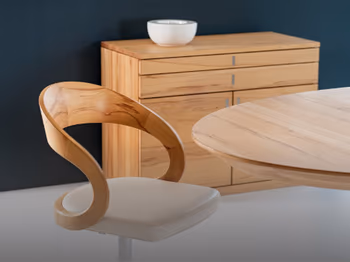Ein Holzstuhl steht an einem Massivholztisch. Im Hintergrund eine Massivholzkommode