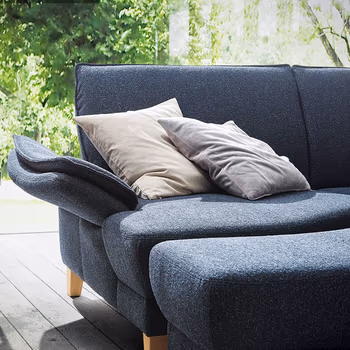 Armlehne eines Blauen Sofas, das vor einem großen Fenster mit Blick ins Grüne steht.