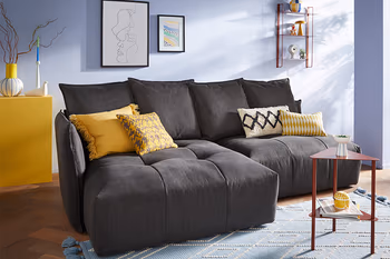 Dunkelgraues Sofa mit vielen Kissen am Rücken und gelben Dekokissen.