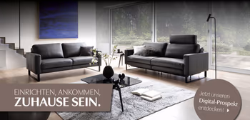 Wohnzimmer mit zwei Sofas; Claim „Zuhause sein“ und Digital-Prospekt-Link.