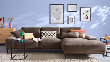 Helles Wohnzimmer mit großem dunkelbraunen Ecksofa und zwei Designder-Beistelltischen und einer Kommode.