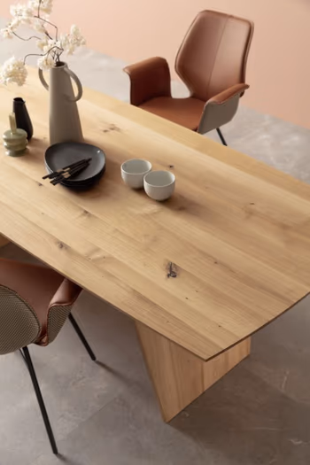 Moderner Esstisch aus Massivholz mit Tischplatte in organischer Form, auf der eine Karaffe, Tassen, Teller und Besteck liegen.