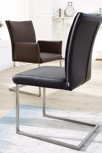 Schwarzer Freischwinger Stuhl mit silbernem Fußgestell, dahinter ein brauner Freischwinger Stuhl mit Armlehne und silbernem Fußgestell.