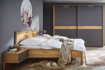 Modernes Holzbett mit am Bett befestigter Nachtkonsole mit grauer Schubladenfront und großem Schwebetürenschrank mit grauen Türen und Holzelement an den Türen.