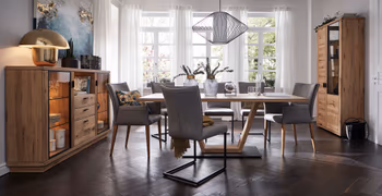 Graue Armlehnstühle und graue Freischwinger mit schwarzem Gestell in einem gemütlichen Esszimmer mit Massivholzmöbeln.