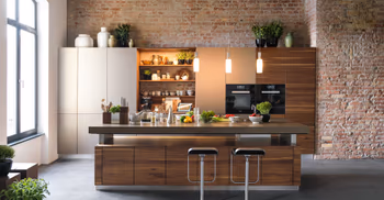 Massivholzküche mit vielen Lebensmitteln/Zutaten auf der Arbeitsplatte. Im Hintergrund ein Ziegelgemäuer.