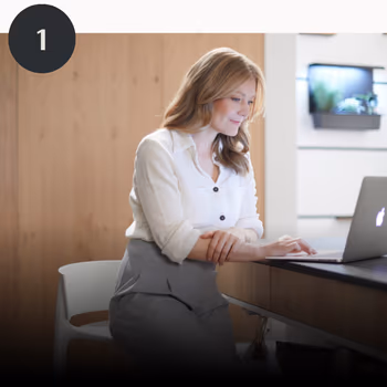 Frau sitzt in einer Holzküche vor dem Laptop.