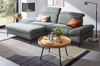 Grünes Ecksofa mit klappbaren Kopfstützen in einem hellen Raum.