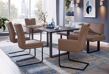 Essgruppe mit braunen Freischwingerstühlen und passender Bank, dazu ein schwarzer Tisch auf einem blauen Teppich in einem modernen Esszimmer mit großen Fenstern.