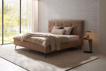 Beiges Polsterbett mit Steppung am Kopfteil in einem hellen Raum.