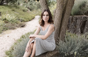 Frau sitzt entspannt vor einem Baum am Boden.