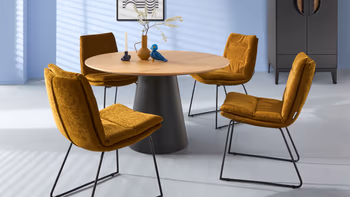 Esszimmer mit einem runden Tisch mit Holzplatte und vier senfgelben Stühlen.