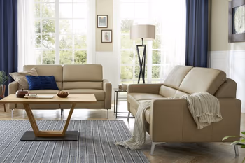 Zwei Ledersofas mit Taupe farbenem Bezug nebeneinander um einen hellen Couchtisch in einem hellen Wohnzimmer.