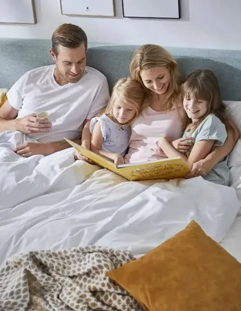 Familie liegt gemütlich in einem grauen Boxspringbett.