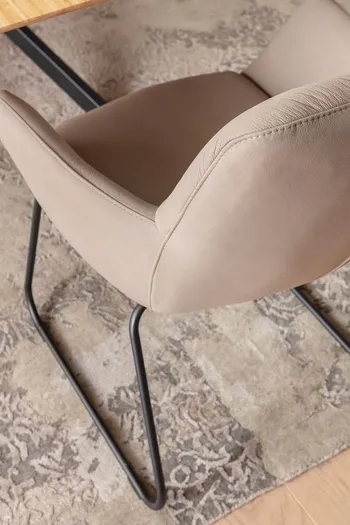 Grauer Schalenstuhl mit schwarzem Metallgestell von oben auf einem hellen Teppich mit dunkler Musterung.