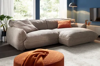 Graues Ecksofa mit bequemer gemütlicher Polsterung in einem hellen Raum mit zwei Hocker.