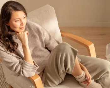 Frau sitzt entspannt mit Kopf auf der Hand gelehnt auf einem Stuhl und blickt in die Ferne.