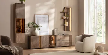 Moderne Wohnwand aus massiver Buche mit beleuchteten Glaseinsätzen in einem hellen Wohnzimmer, in dem ein heller Sessel, heller Teppich und helle Dekoration sind.