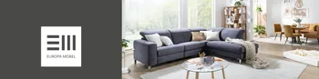Blaues Stoffsofa in einem modernen, gemütlichen Wohnzimmer. Im Hintergrund sieht man eine Essgruppe in Braun. Auf der linken Seite ist das Europa Möbel Collections Logo auf einer grauen Fläche.&nbsp;