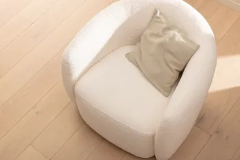 Runder Sessel mit niedriger Rückenlehnemit cremefarbenem Stoffbezug, auf dem ein beiges Kissen liegt.