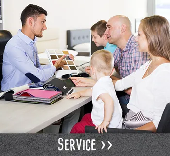 Beratungssituation mit einer Familie am Tisch, ein Verkäufer zeigt Stoffmuster.