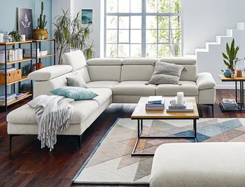 Weisses Stoffsofa mit hoelzernem Couchtisch in gemuetlichem Wohnzimmer mit Kissen und Decke.