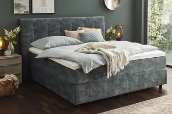 Graues Boxspringbett mit rautensteppung am Kopfteil in einem hellen Schlafzimmer.