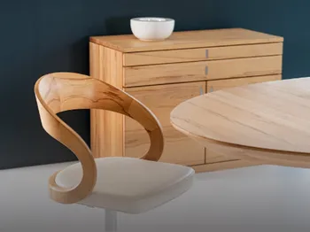 Ein Holzstuhl steht an einem Massivholztisch. Im Hintergrund eine Massivholzkommode