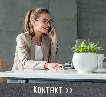 Freundliche Frau im Business-Outfit telefoniert an einem modernen Schreibtisch mit Laptop und Pflanze.