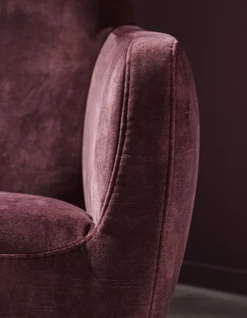 Armlehne eines Sessels, der mit Stoff in Beere bezogen ist.
