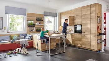 Familienfreundliche Wohnküche mit Holzfronten, Sitzbank am Fenster, Spielzeug auf dem Boden und gemütlicher Atmosphäre.