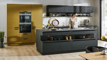 Moderne Designküche mit goldfarbener Gerätewand, dunkler Kücheninsel und stilvoller Einrichtung, Frau bereitet Kaffee zu.