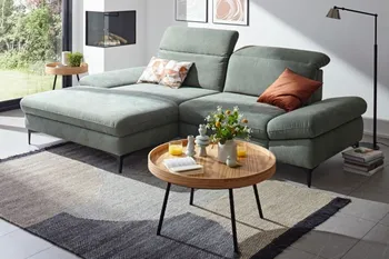 Grünes Ecksofa mit klappbaren Kopfstützen in einem hellen Raum.