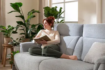 Frau liegt auf einem hellgrauen 2-Sitzersofa und liest ein Buch.