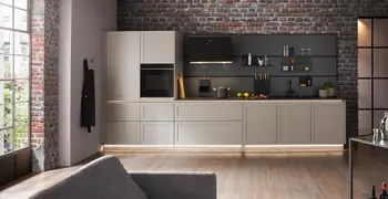 Moderne beige Küche vor einer dunklen Backsteinwand.