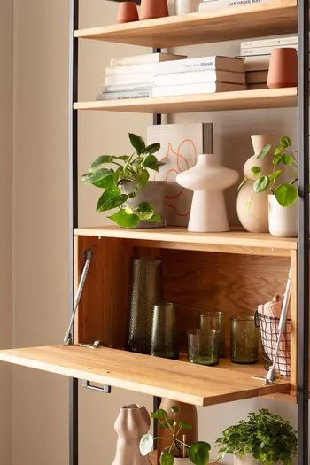 Regal mit schwarzem Rahmen aus Metall und hellen Holzeinlegeböden, dekoriert mit vielen hellen Vasen und Pflanzen und Büchern.