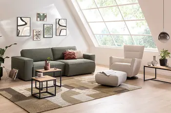 Helles Wohnzimmer mit dunkelgrünem Sofa und weißem Sessel mit passendem Hocker.